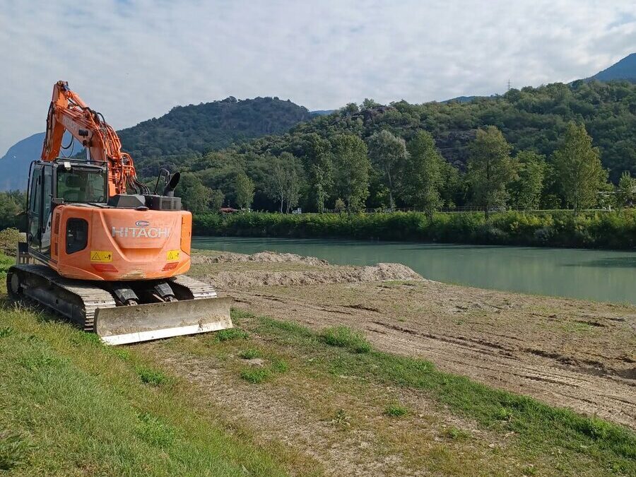 Escavatore cingolato al lavoro sulla sponda dell'Adige a Egna, con la golena ridotta a terra nuda